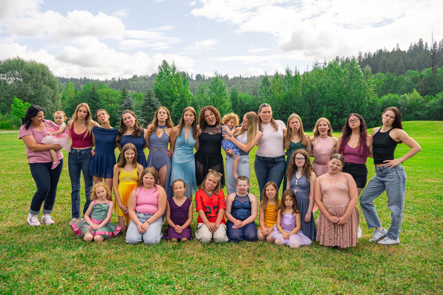 Large group of people posing together on a grassy hillside with trees and mountains in the background.