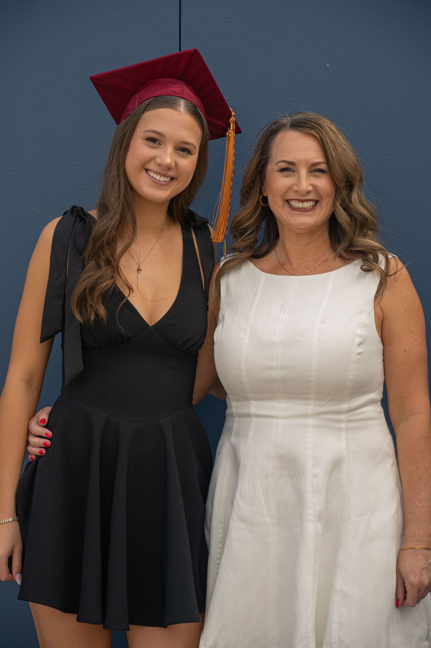 Two graduates pose together in contrasting black and white dresses during a graduation ceremony.
