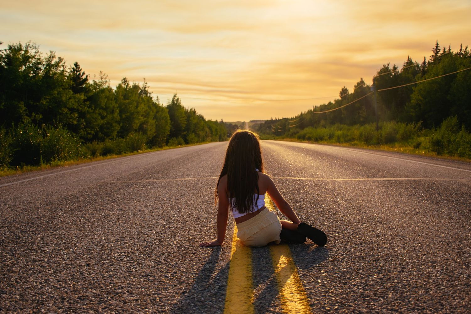 Person sitting in the middle of an empty road during golden hour sunset.