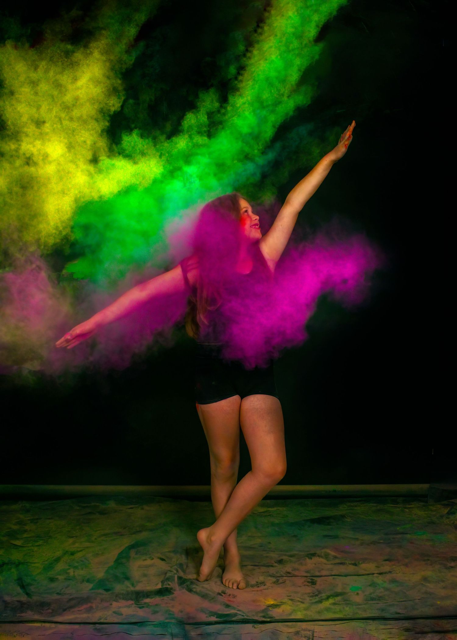 Dancer in black outfit moving through vibrant green and pink powder clouds.