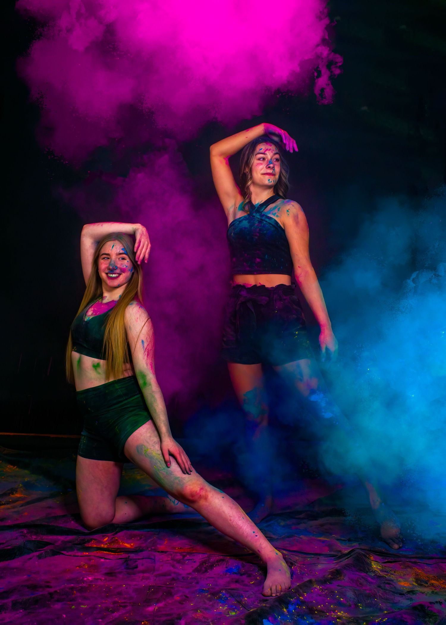 Dancers pose dramatically amid colorful pink and blue smoke on a dark stage.