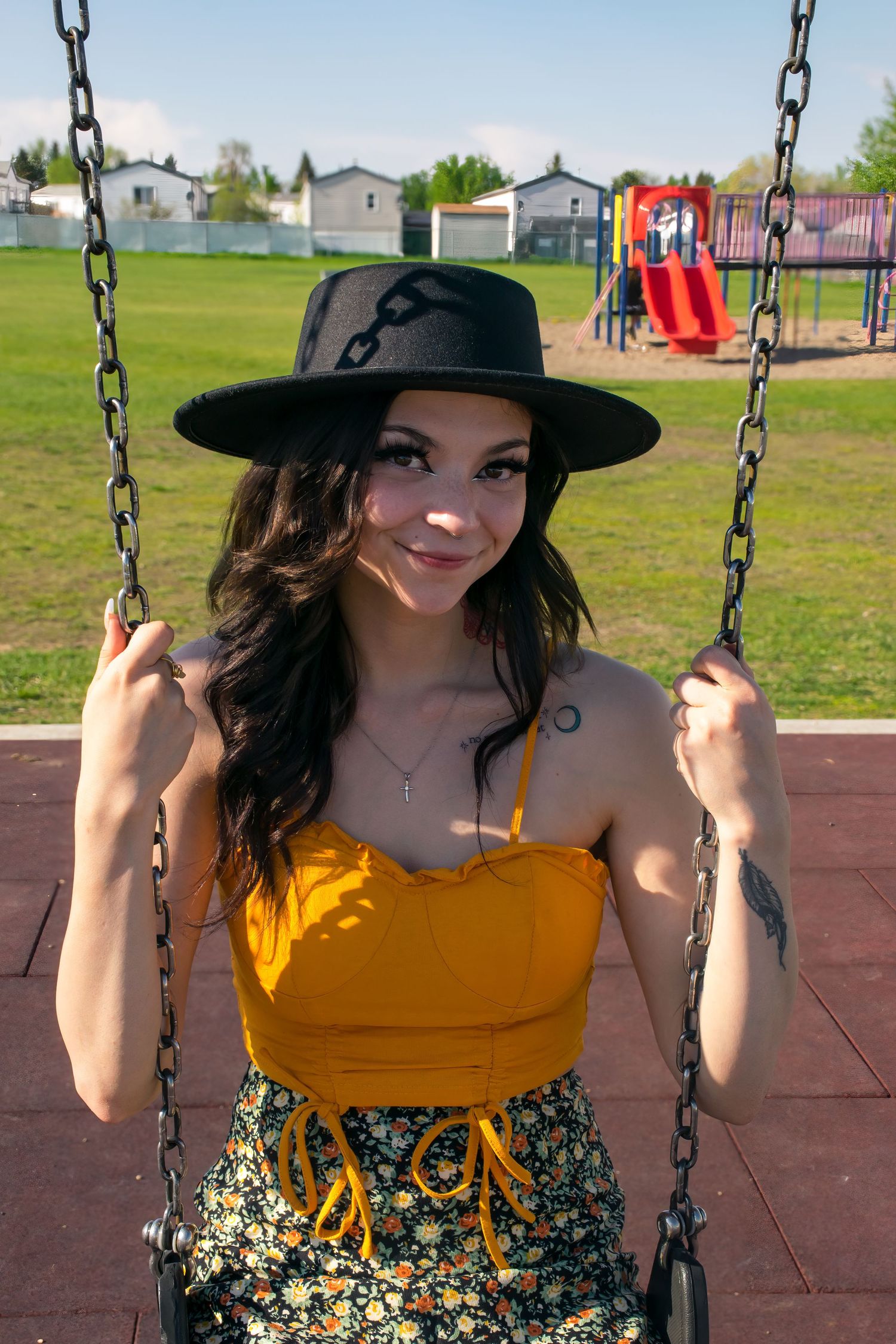 A person in a yellow top and hat sits on a playground swing on a sunny day.