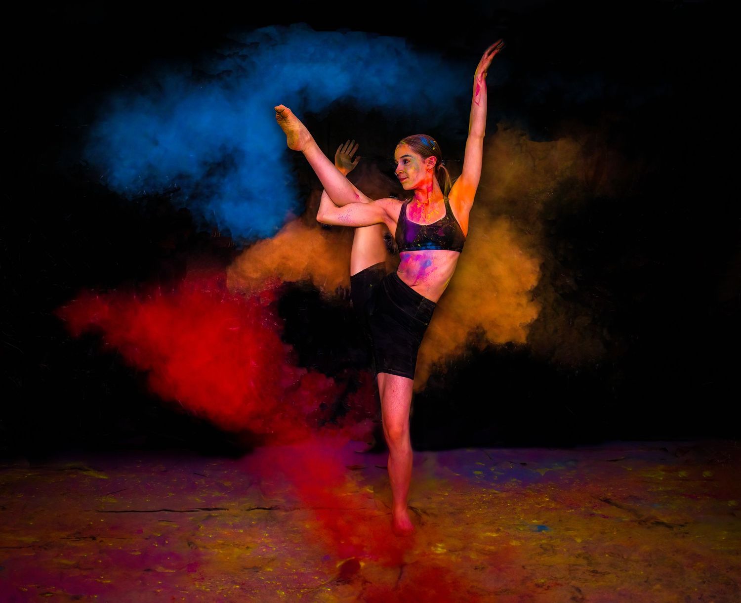 Dynamic dance pose captured with red and blue powder effects creating dramatic contrast.