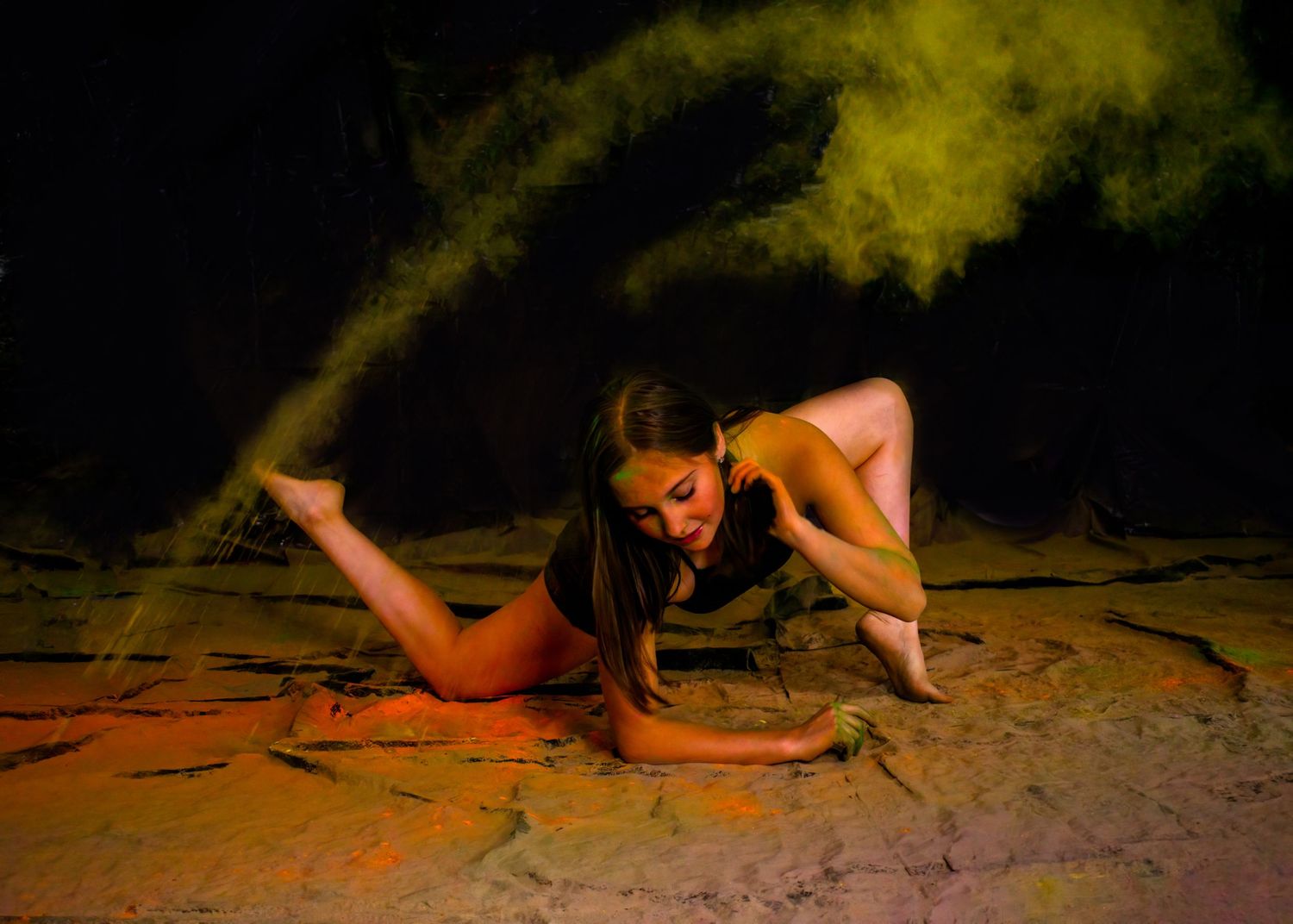 Dancer in dynamic low pose surrounded by ethereal yellow smoke effects.