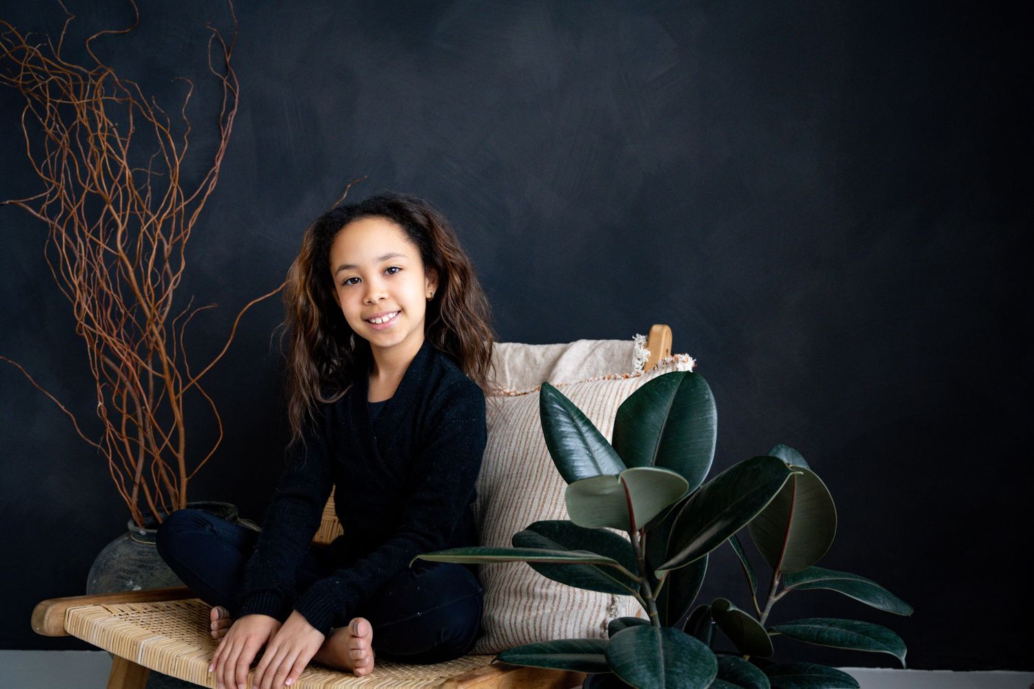 Person in black sits relaxed on bench with decorative plants against dark backdrop.