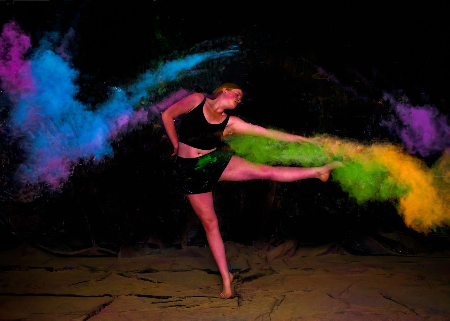 A dancer executing a high kick with rainbow colored powder effects in motion.