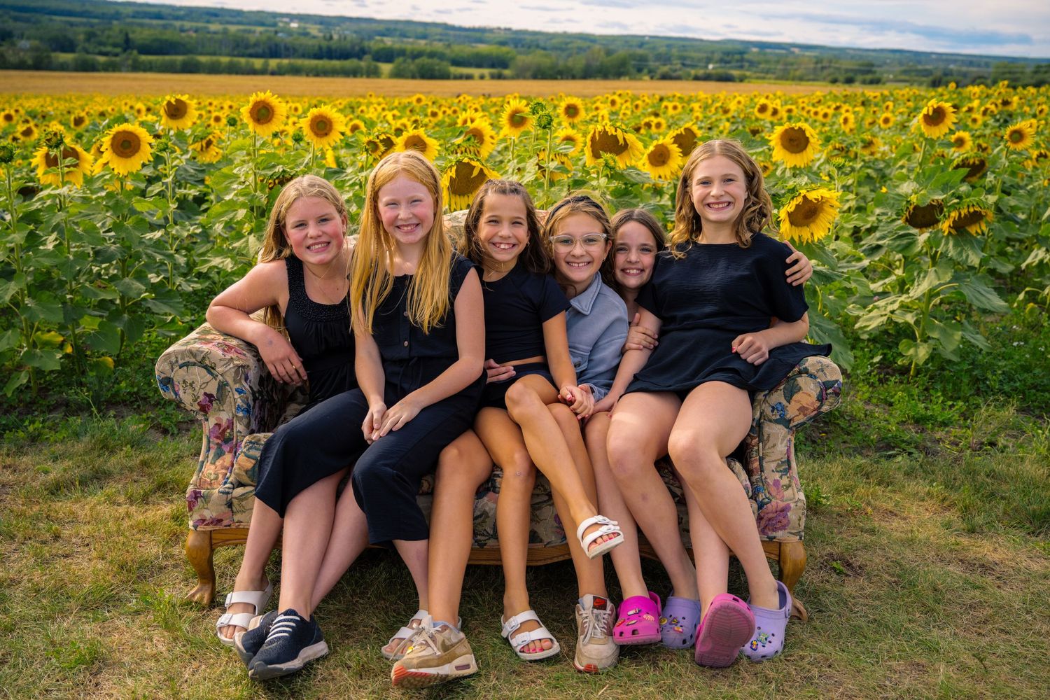 A group seated on a couch in front of a vibrant sunflower field on a summer day.