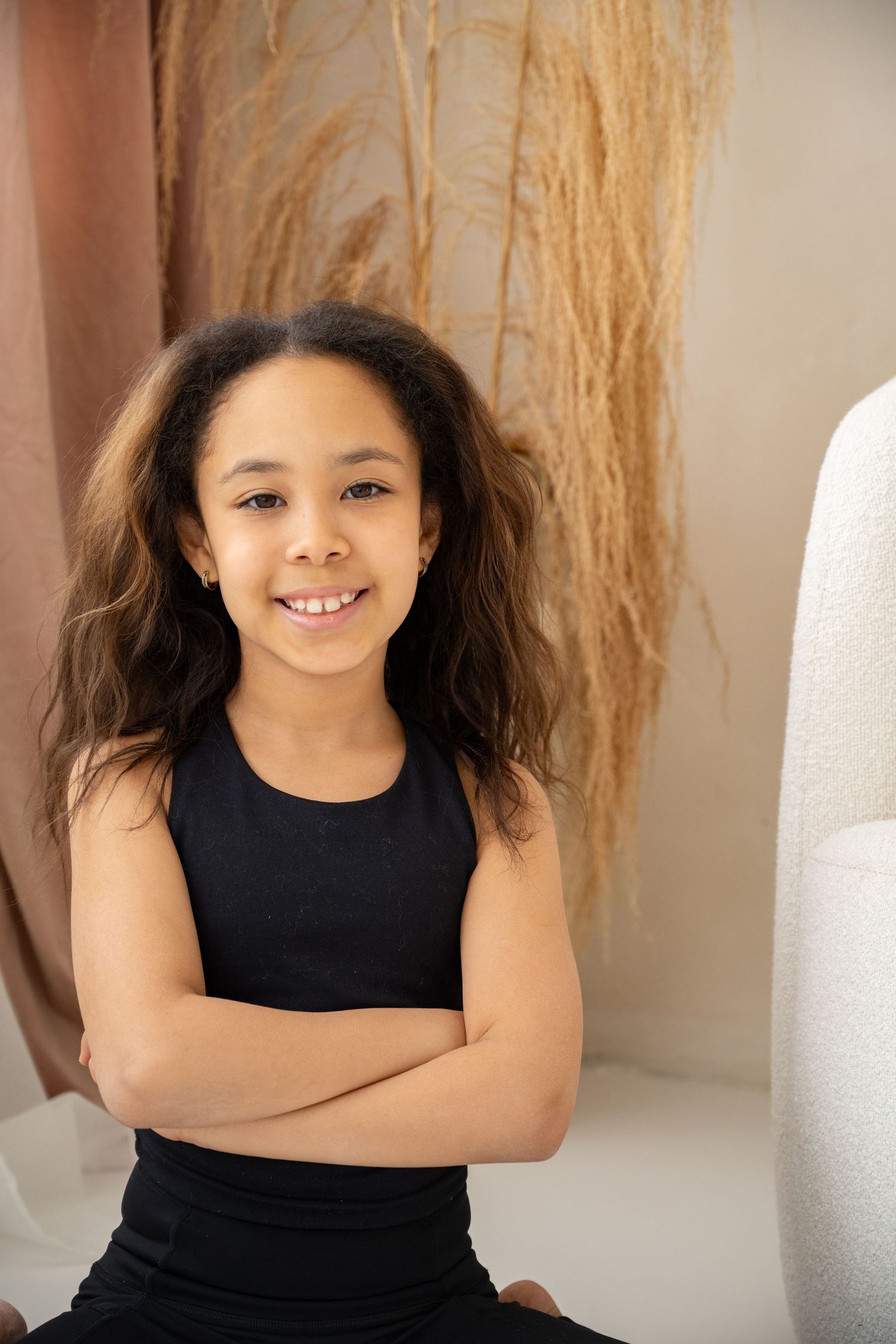 Young dancer in black tank top sitting with confident pose against neutral background.