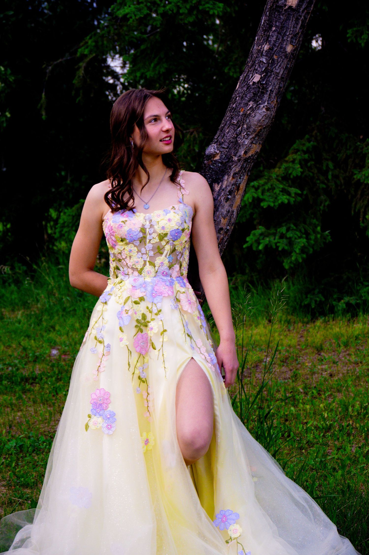 A soft yellow and lavender floral tulle gown glows ethereally against a lush forest backdrop during outdoor photos.