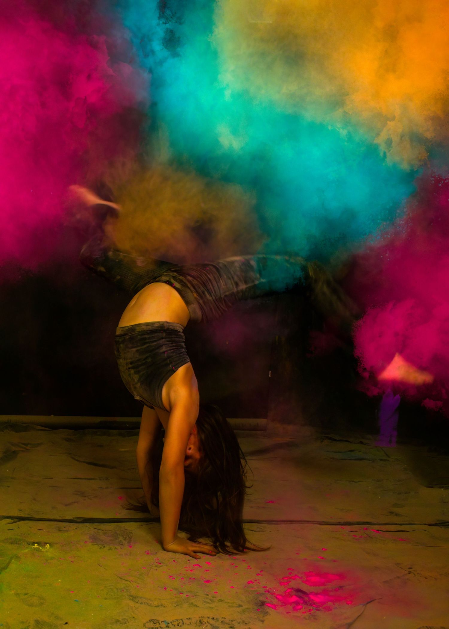 Dancer performing backbend against colorful powder explosion background.