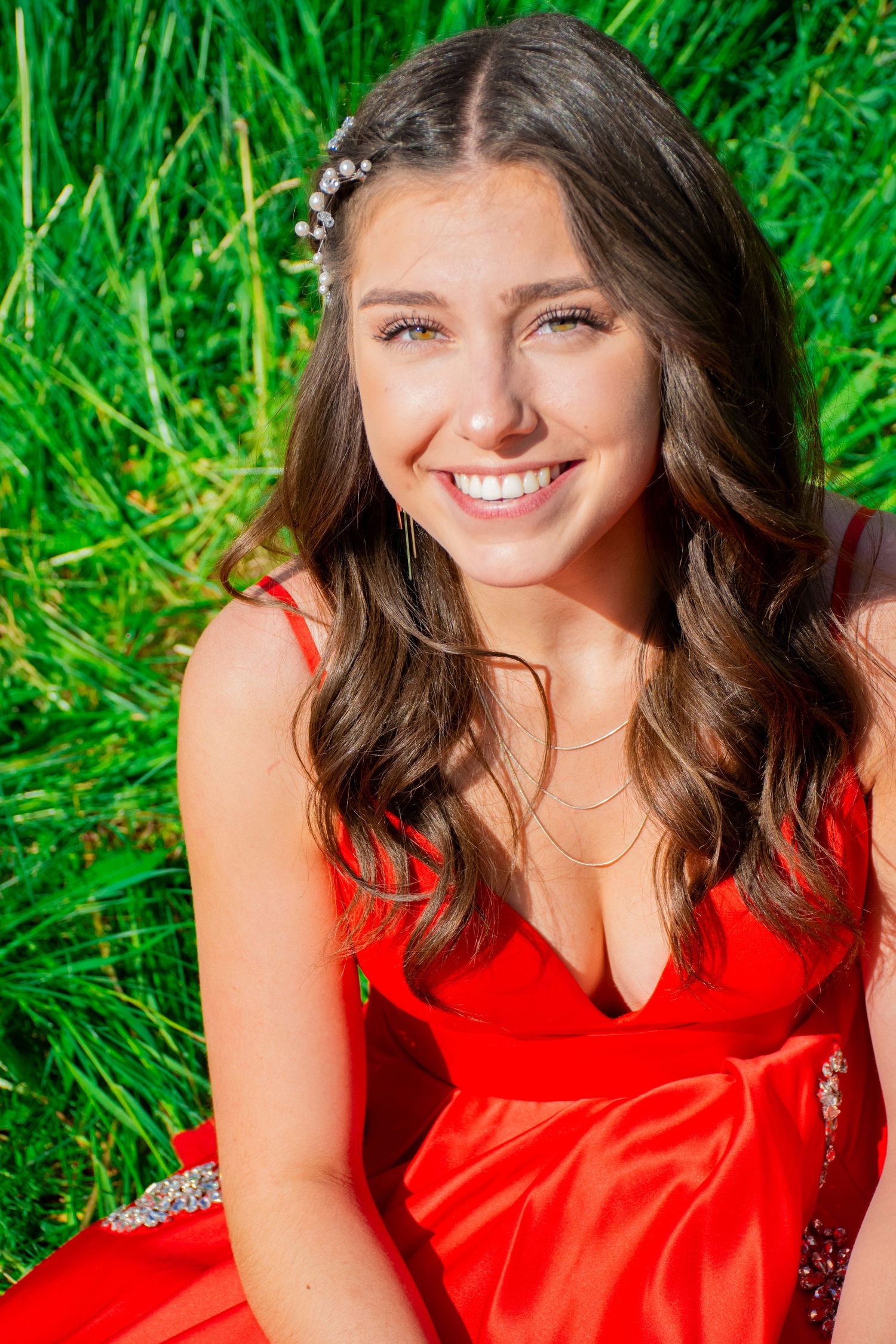 Portrait in vivid red dress against lush green natural backdrop.