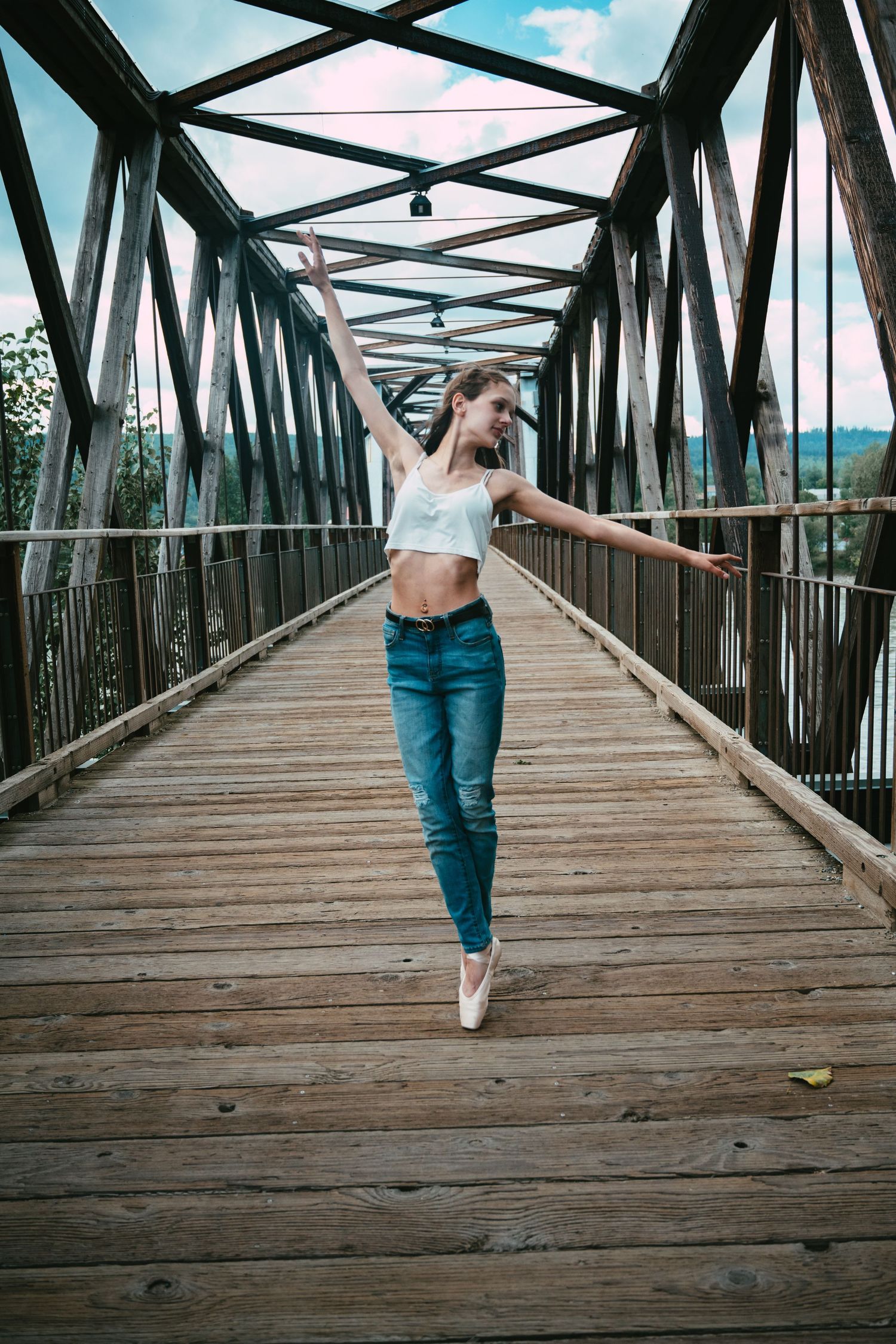 Dance pose on wooden bridge with industrial metal frame structure.