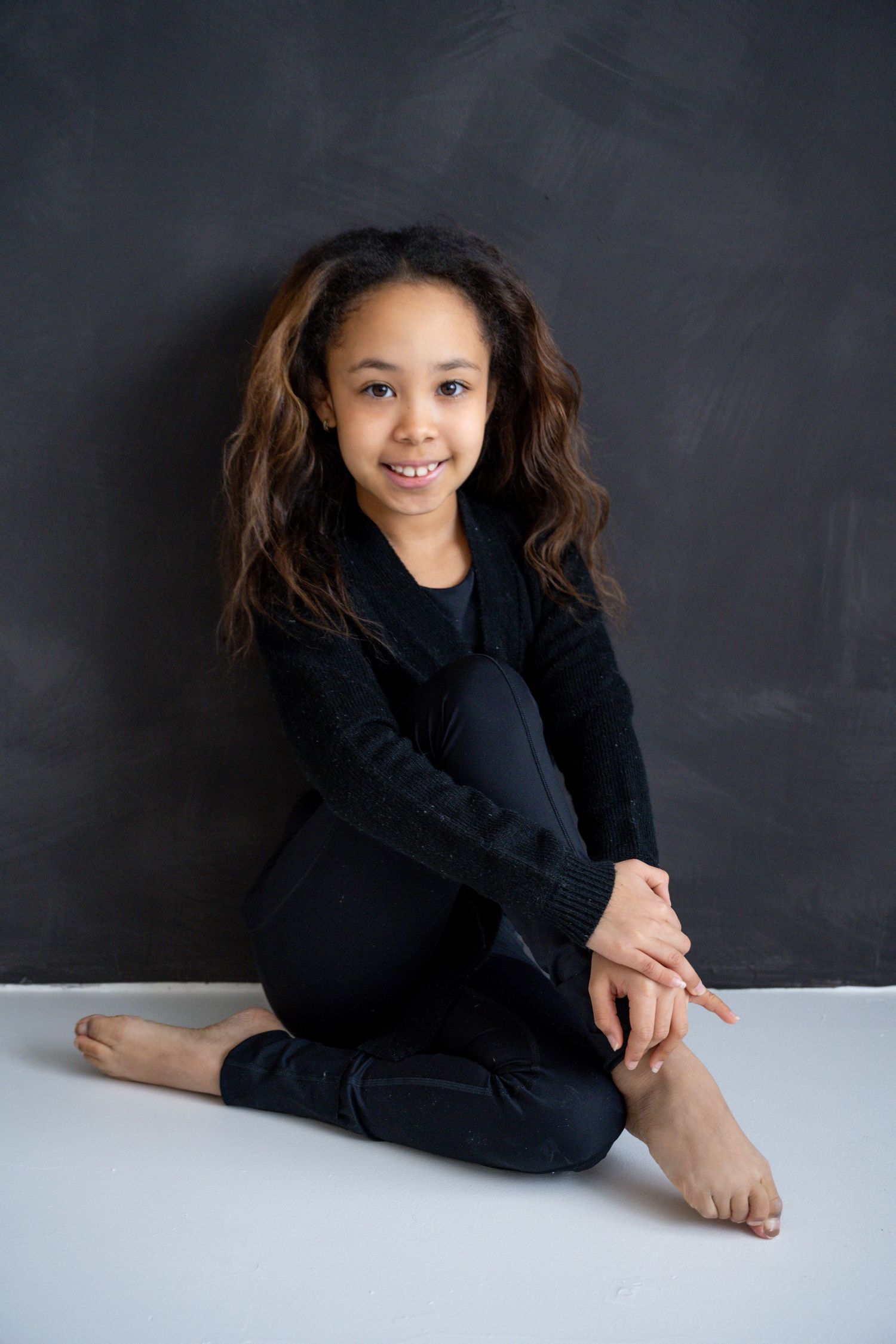 Portrait against a chalkboard background featuring casual dark clothing and natural styling.