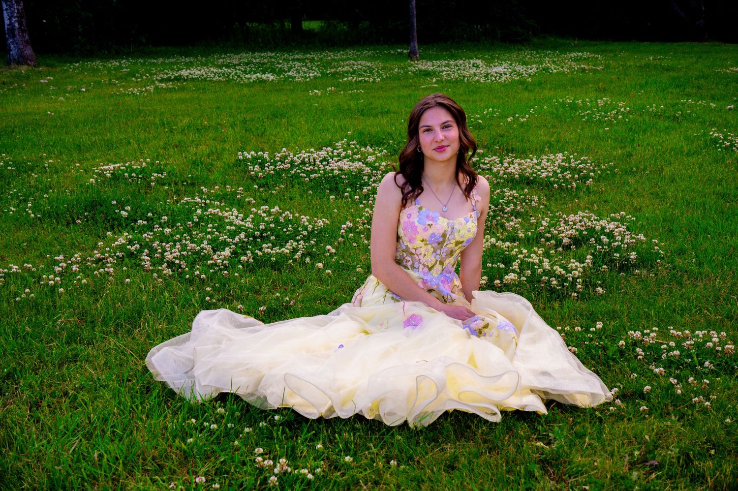 Someone in a floral dress sits in a meadow filled with small white wildflowers on a spring day.
