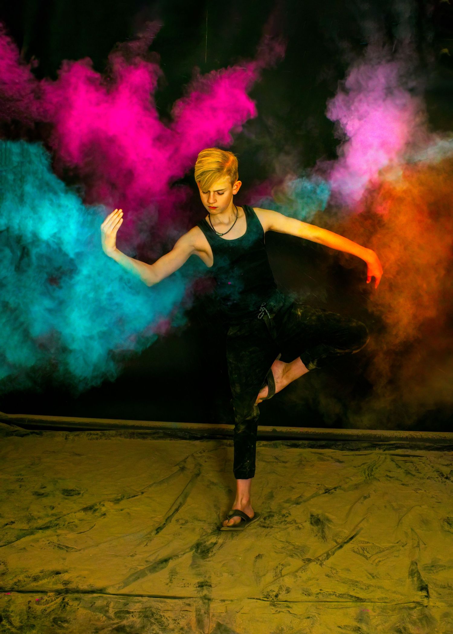 Dancer performing in black outfit amidst colorful powder clouds of pink, orange and turquoise.