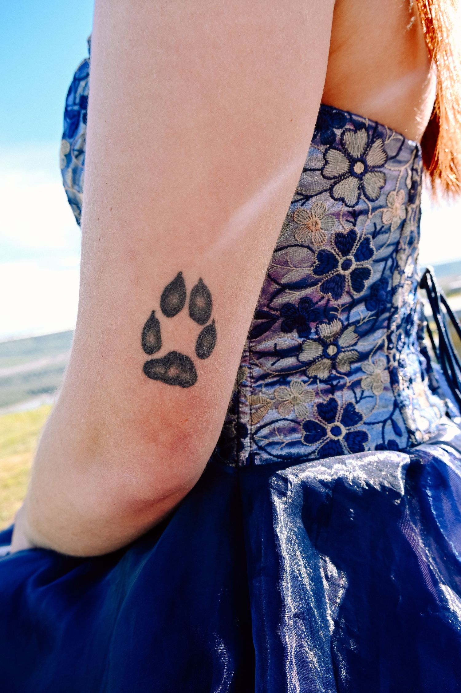 Close-up of paw print tattoo on arm against floral print dress background.