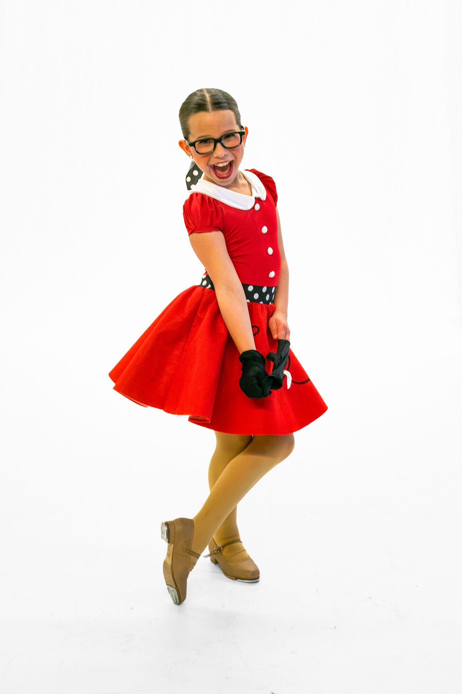 A dancer in a vintage-style red dress and glasses strikes a playful pose against a white background.