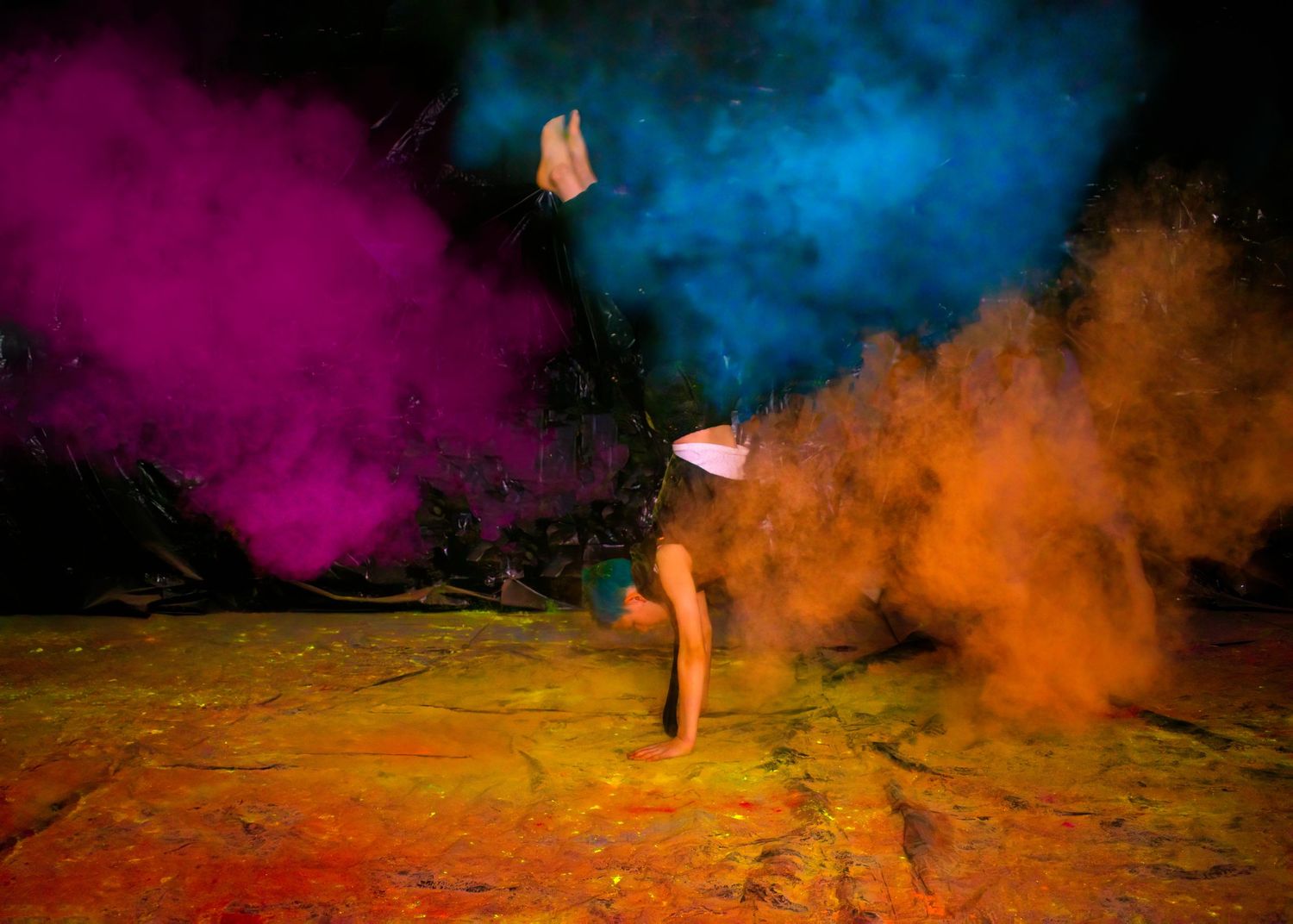 Athletic dance pose surrounded by vibrant orange, pink and blue powder clouds.
