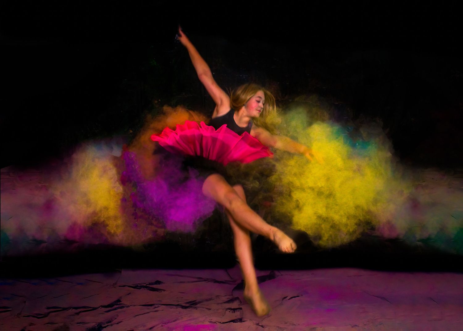 Dancer in motion captured with colorful powder effects against black background.