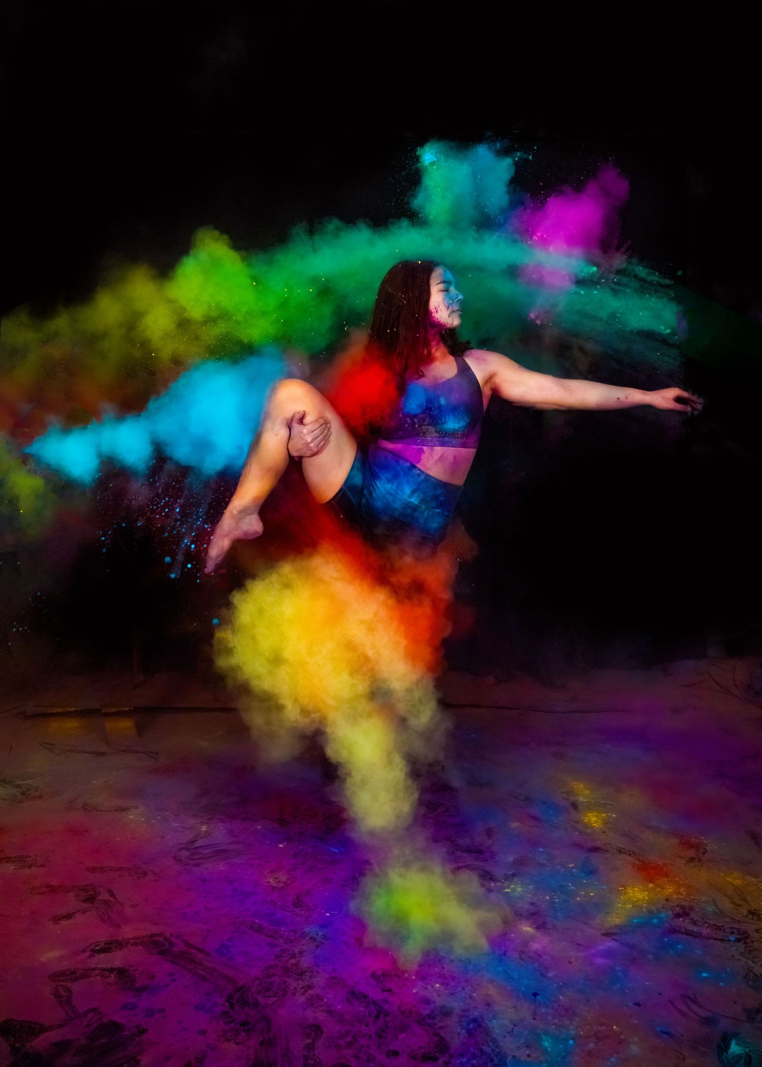 Dancer performs in colorful powder paint explosion against black background.
