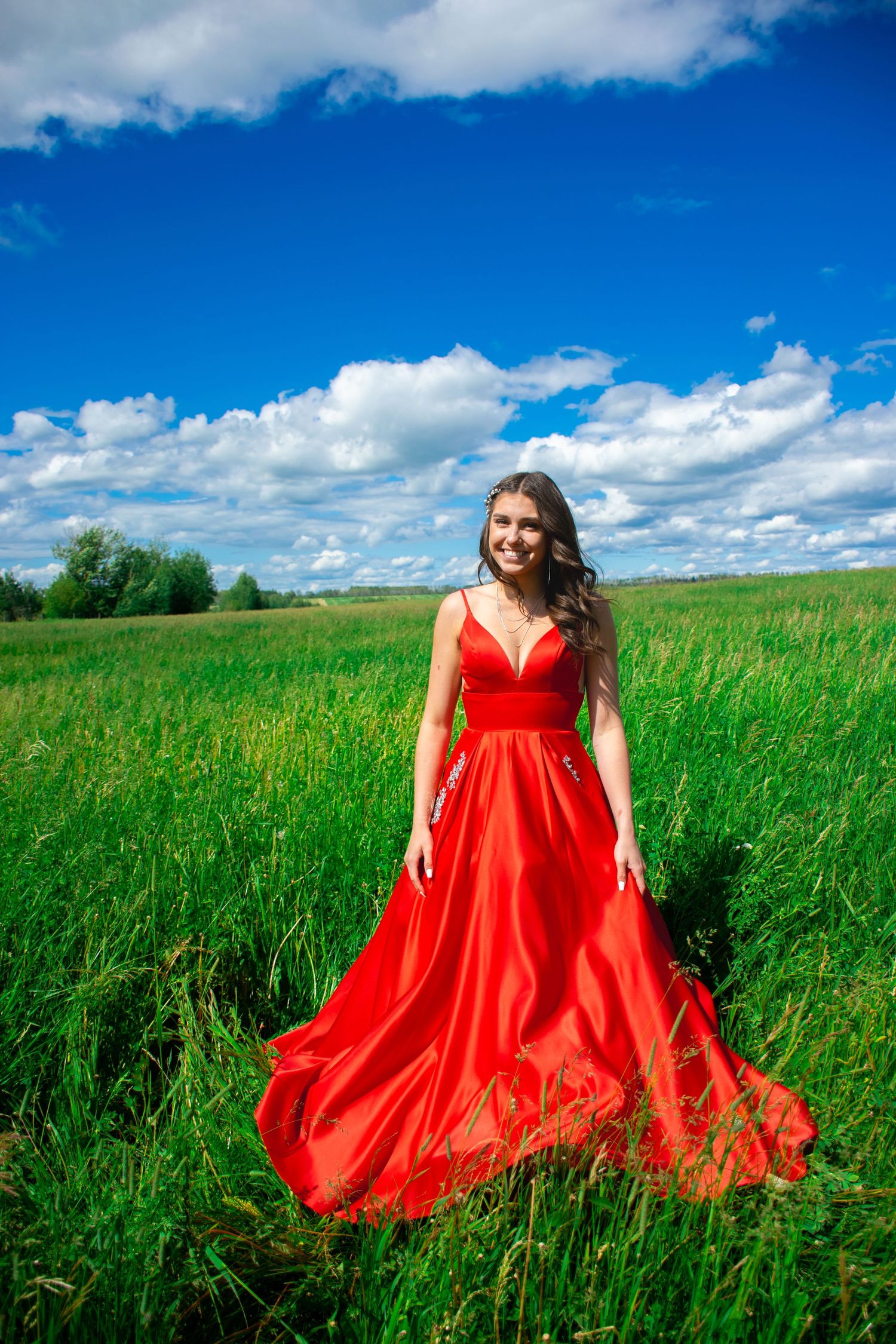 Flowing red gown creates dramatic contrast against green field and blue sky.