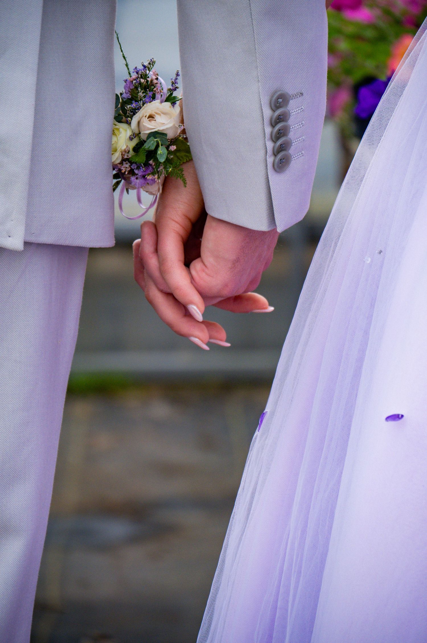 A wedding couple holds hands in a romantic pose showing white dress and gray suit details.