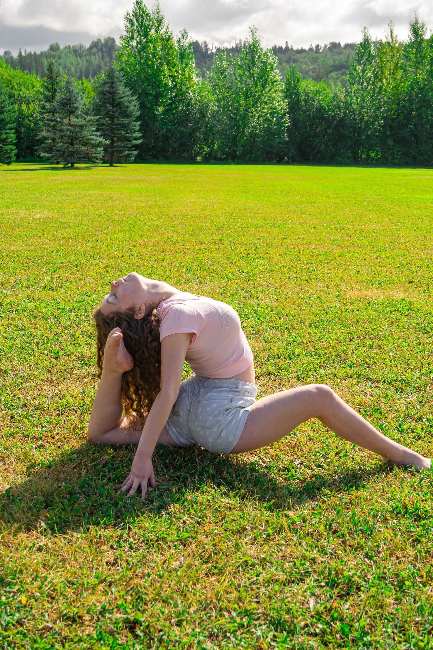 Person somersaulting in sequence across a sunny grass field with trees in the background.