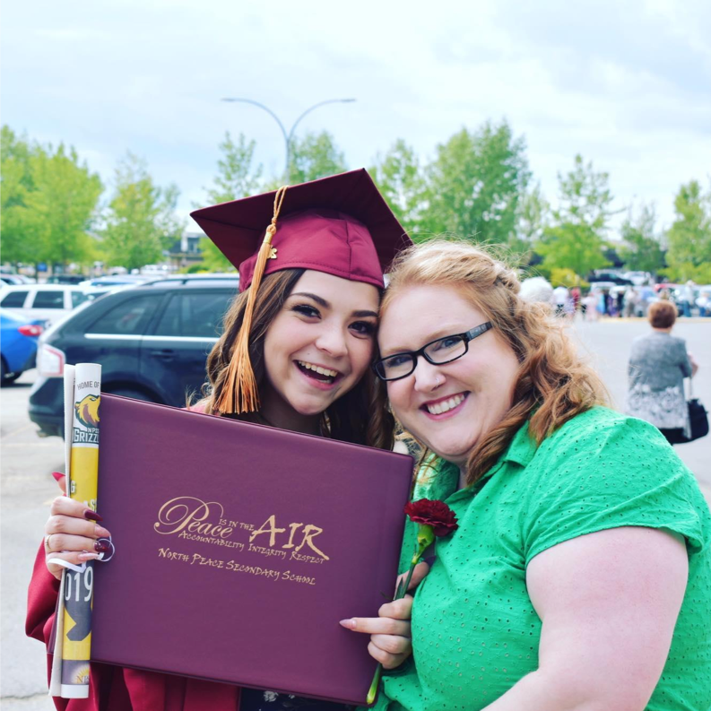 Two friends celebrate at a graduation ceremony with a diploma.