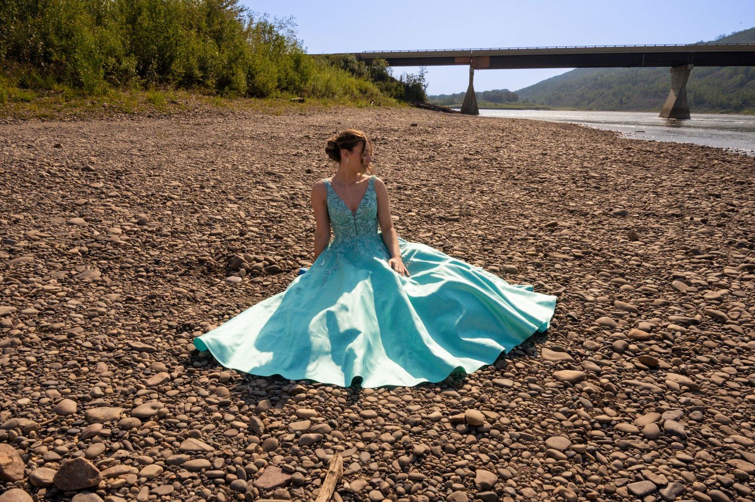 A flowing turquoise dress billows dramatically across a rocky beach landscape at sunset.
