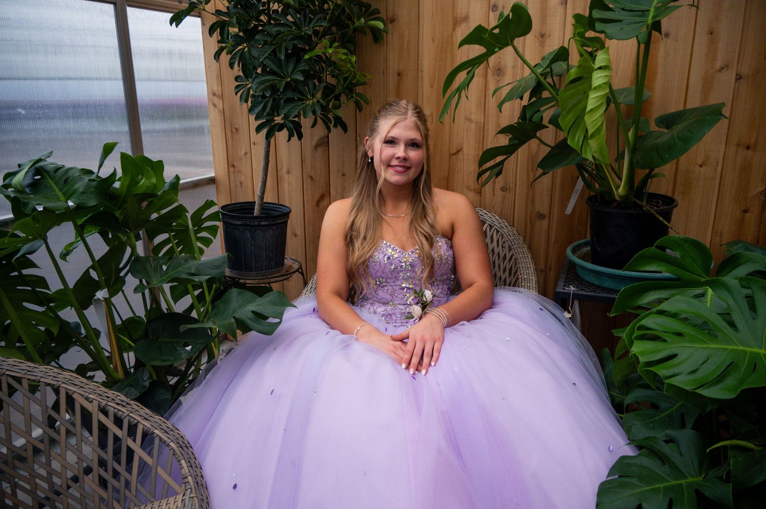 A lavender tulle dress billows out in front of a wooden fence surrounded by lush greenery.