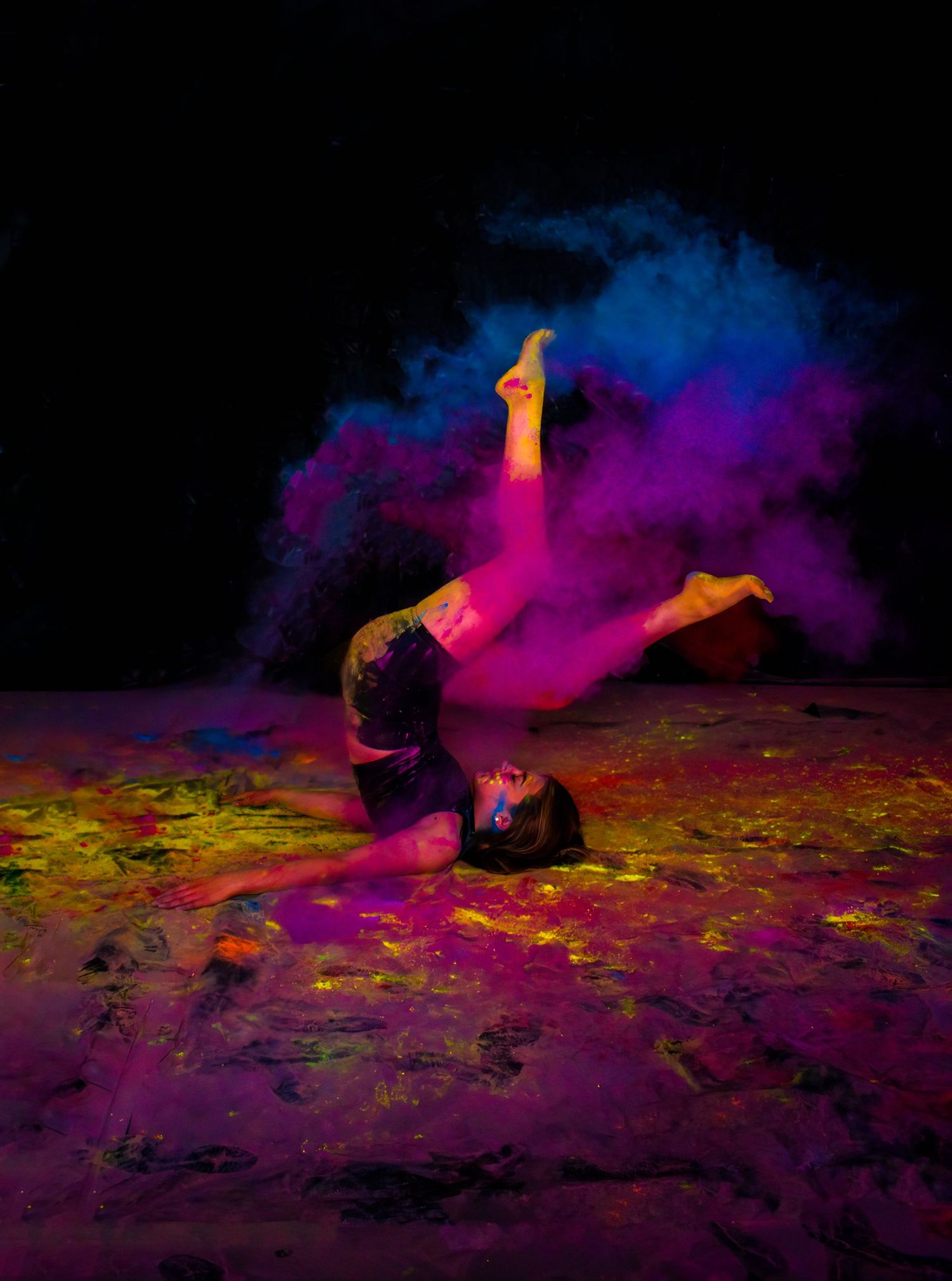 An acrobatic dance move captured with vibrant purple and blue powder effects.