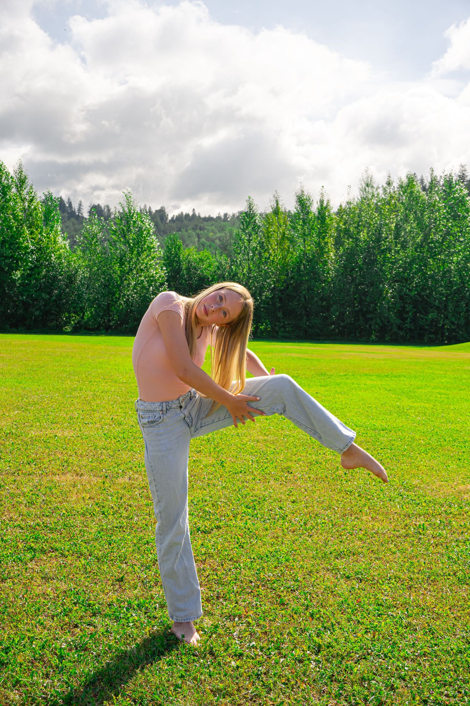 Figure doing cartwheels on green grass with forest trees and cloudy sky in the background.