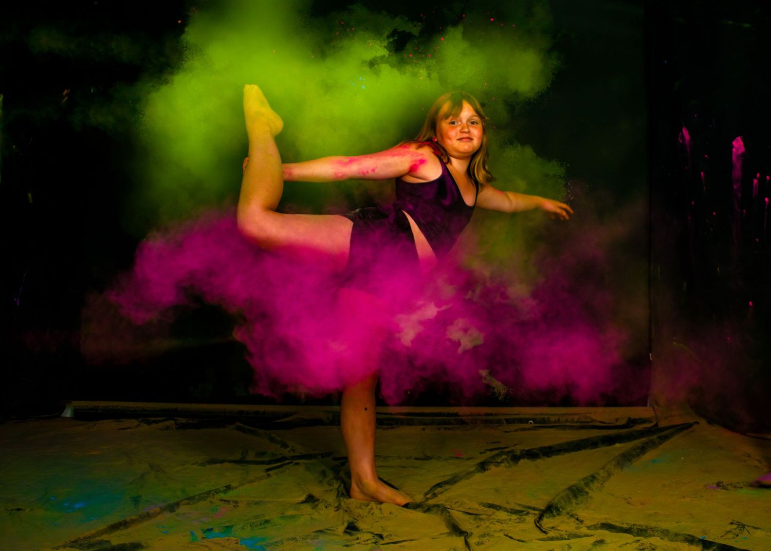 Dynamic dance pose captured with green and pink powder effects in dark studio setting.