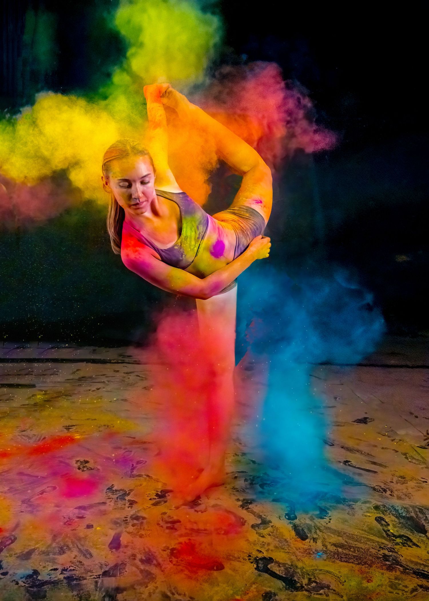 Dancer performs in colorful powder explosion with vibrant yellow, orange and blue hues against dark background.