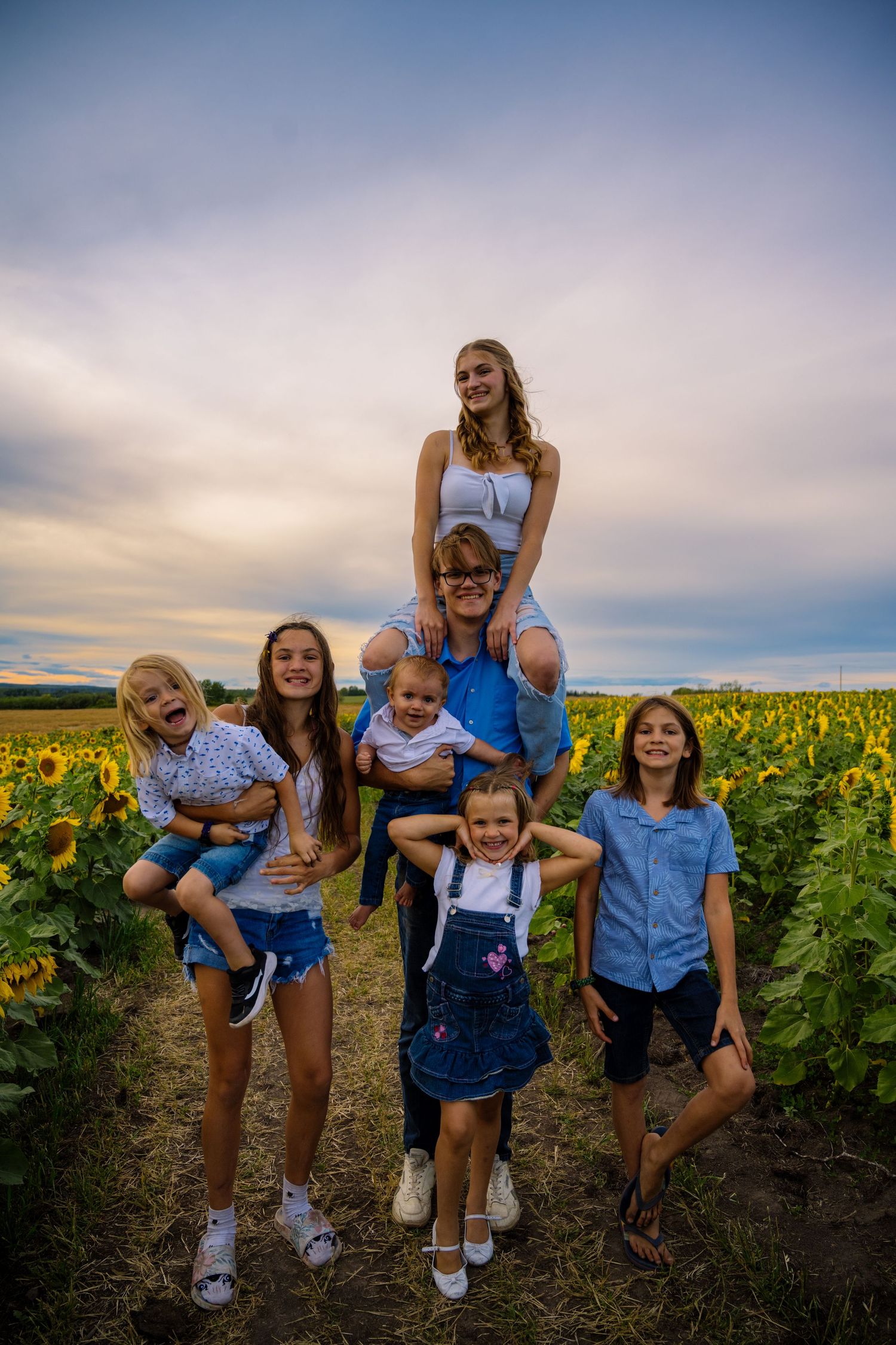 Group poses playfully together in a sunflower field at sunset.