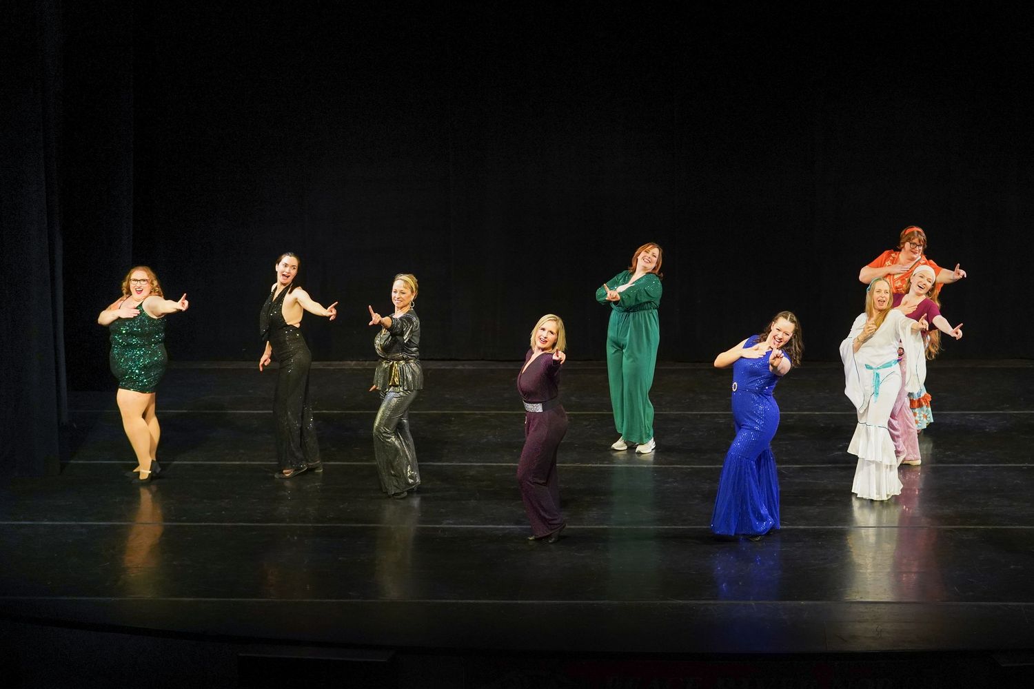 Performers in colorful outfits dance on a dark stage during a show.
