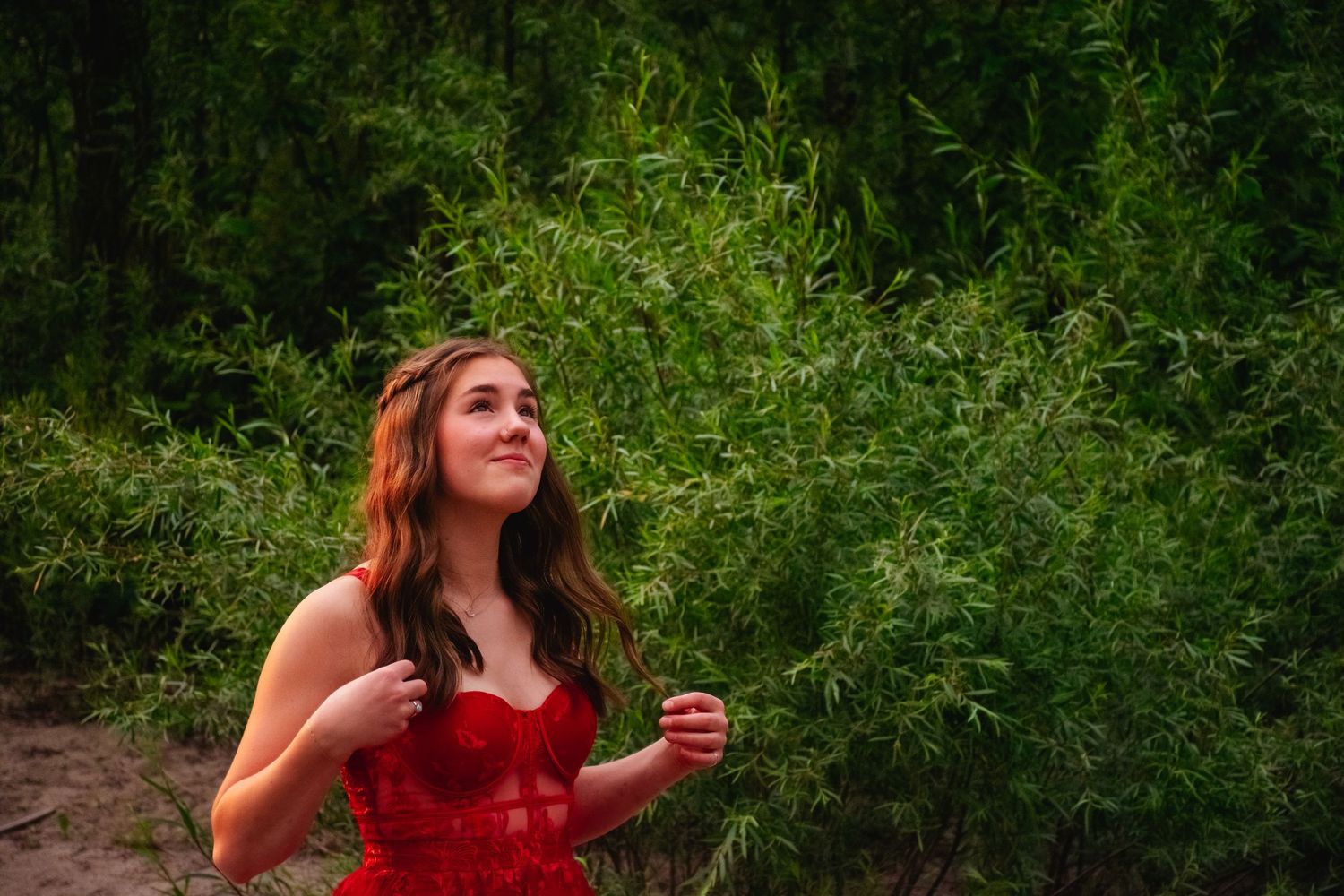 Person in red dress poses against lush green foliage background.