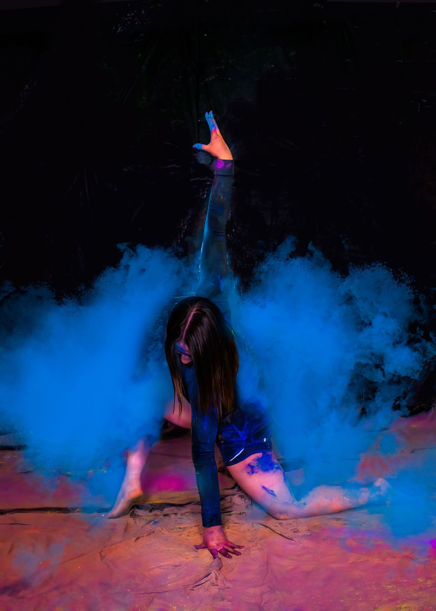 Dancer creates dramatic pose amid swirling blue smoke effects on dark backdrop.