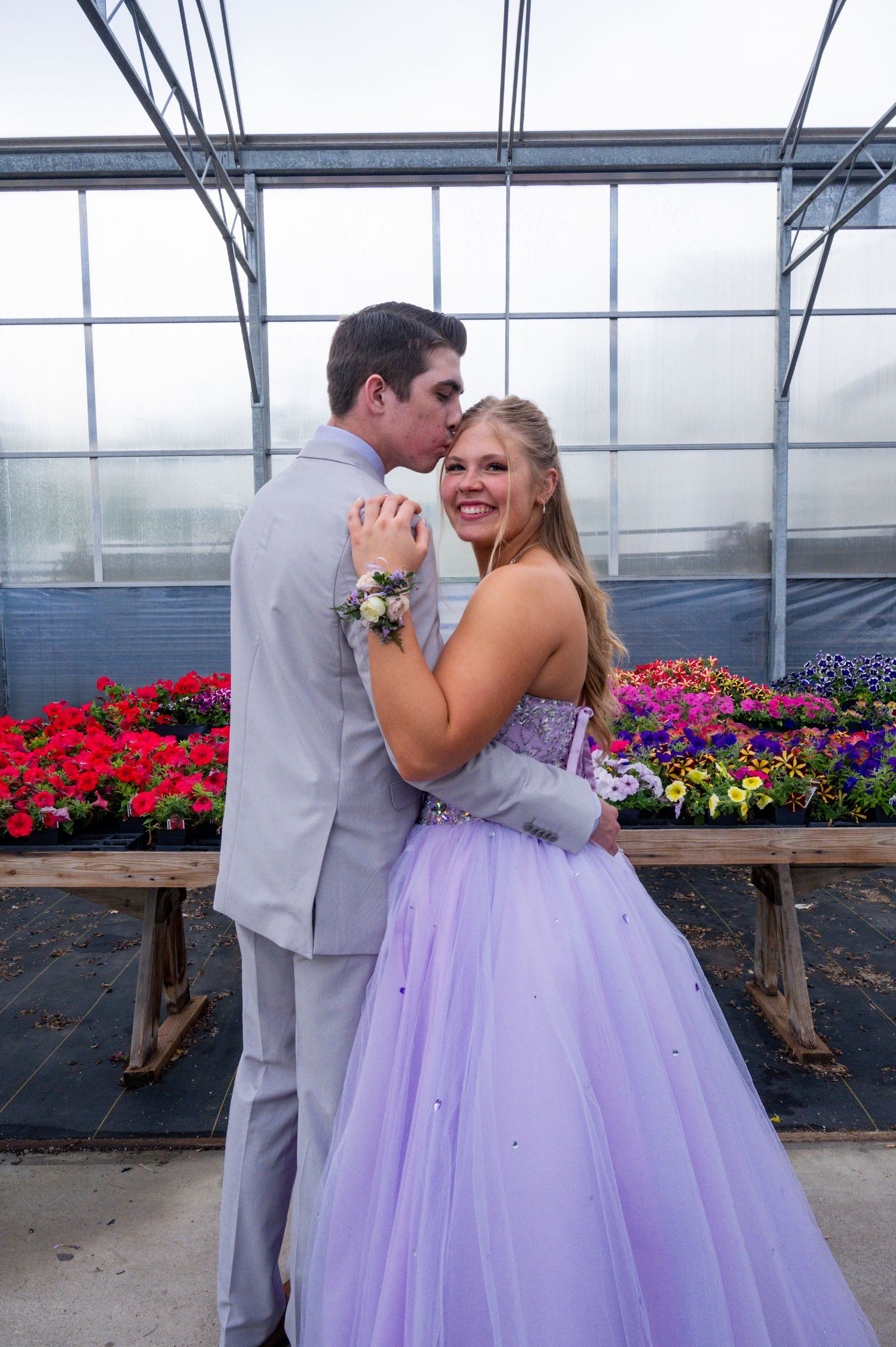 A couple dances together in a greenhouse during a photoshoot surrounded by colorful flowers and benches.