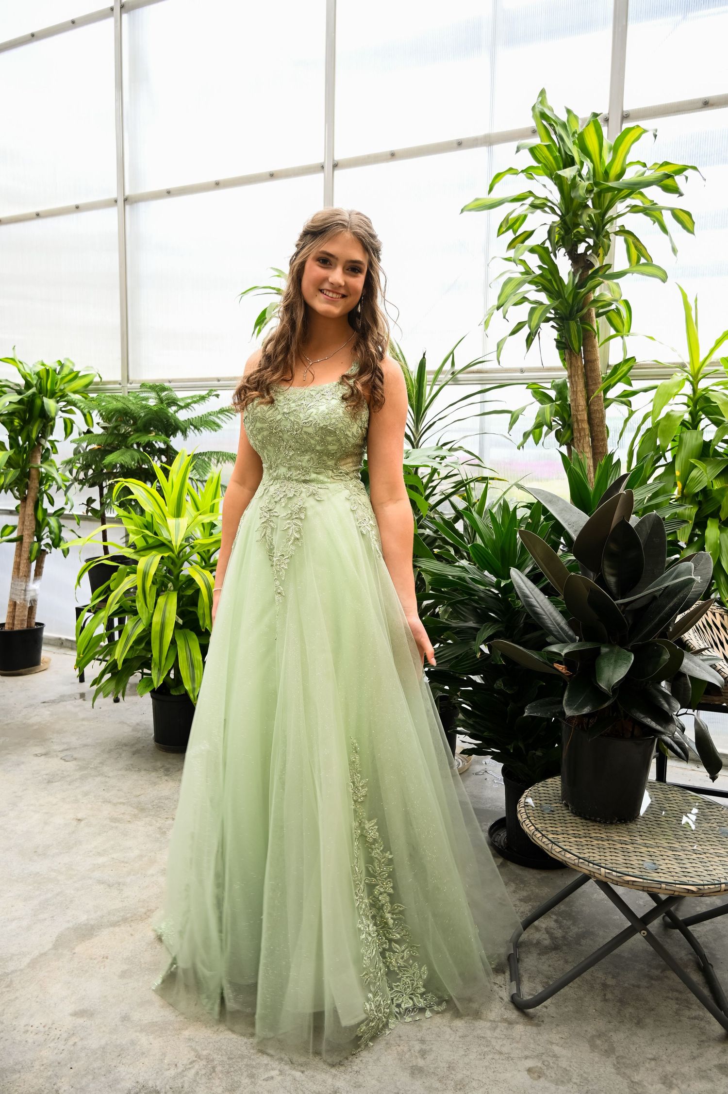 A formal portrait in a greenhouse featuring a long mint green tulle gown among tropical plants.