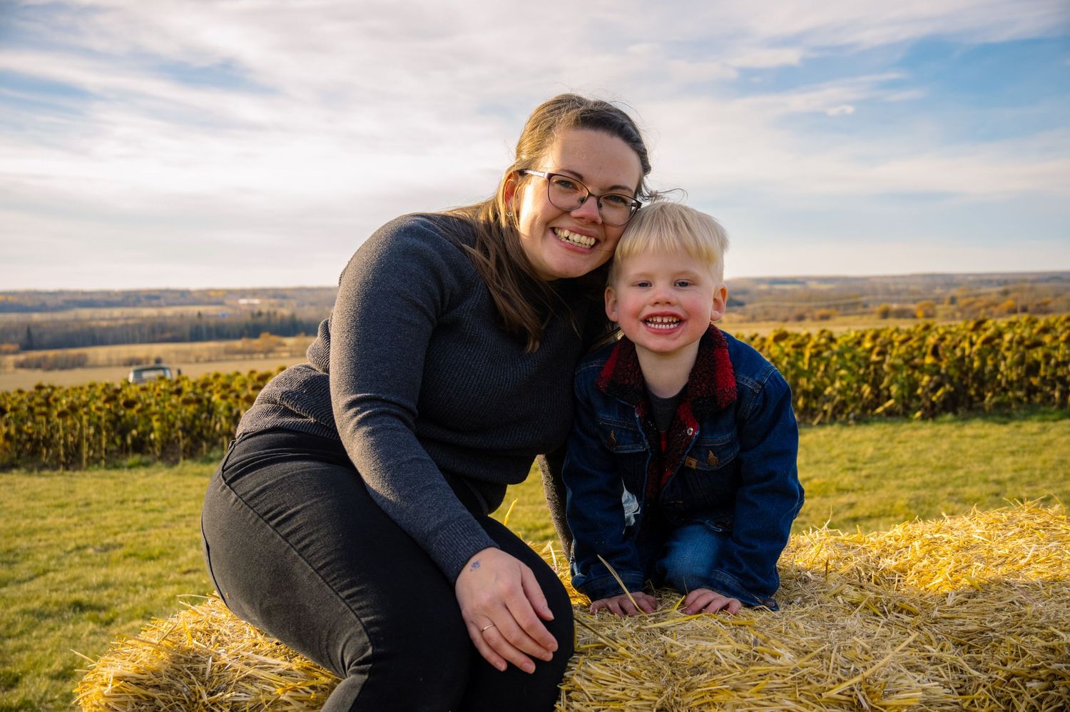 Family moment captured on hay bale with autumn vineyard landscape in background.