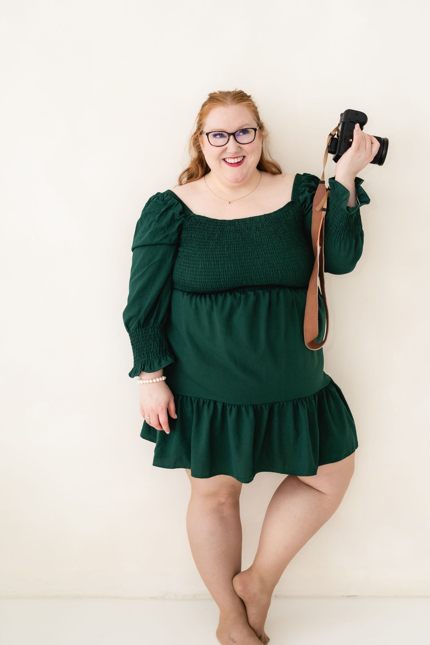 Professional photographer in a green dress holding a camera against a white background.