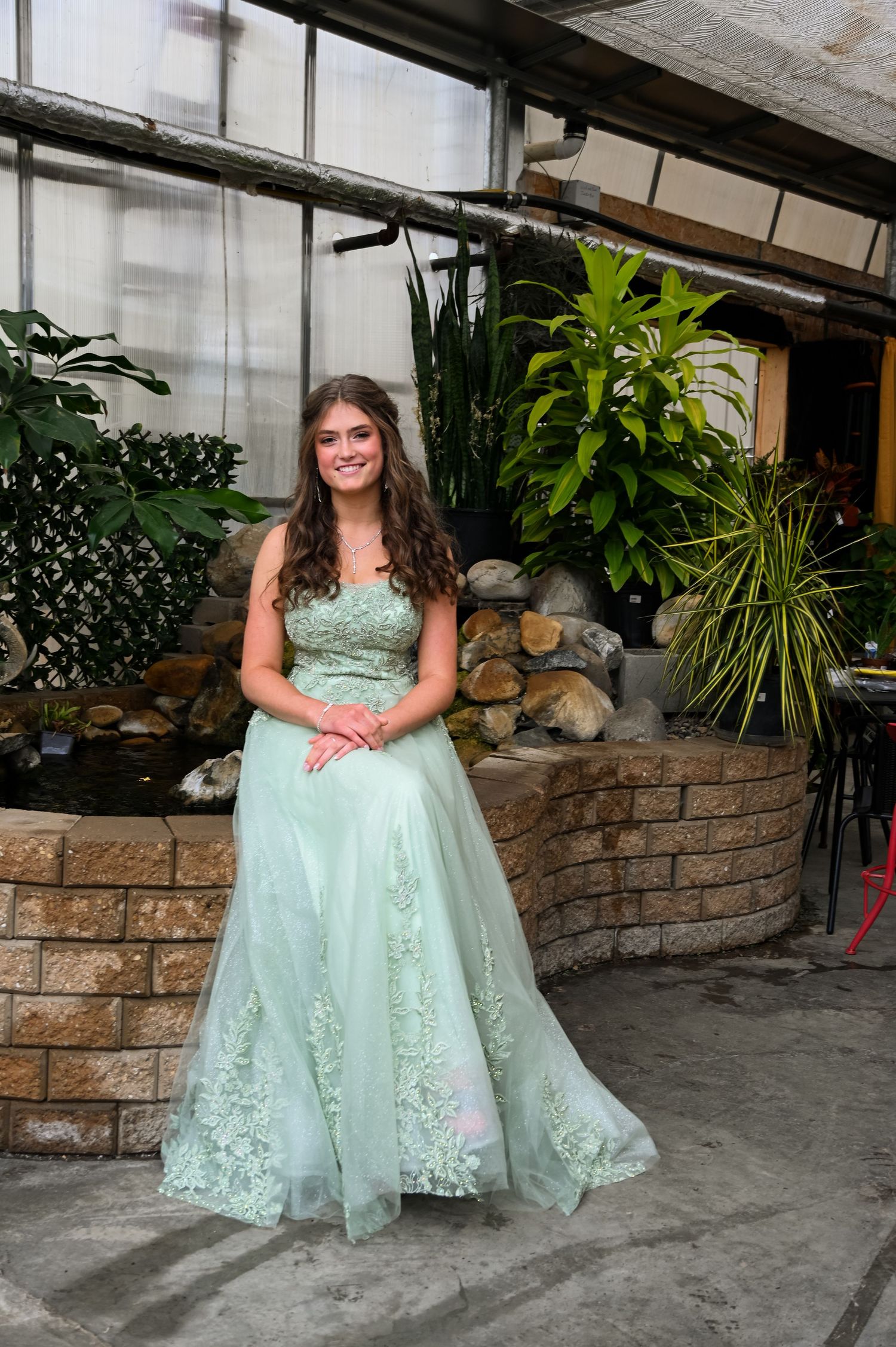 Person in a mint green formal gown poses in front of an indoor garden with tropical plants.