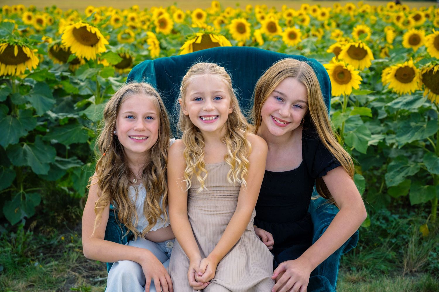 Three friends pose together in a bright sunflower field on a sunny day.