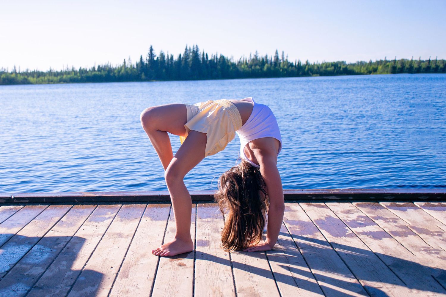 child doing a back bend on a dock in front of the water.