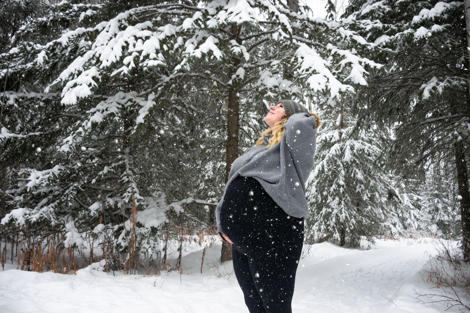 A person stands in a snowy forest while snowflakes fall around them.