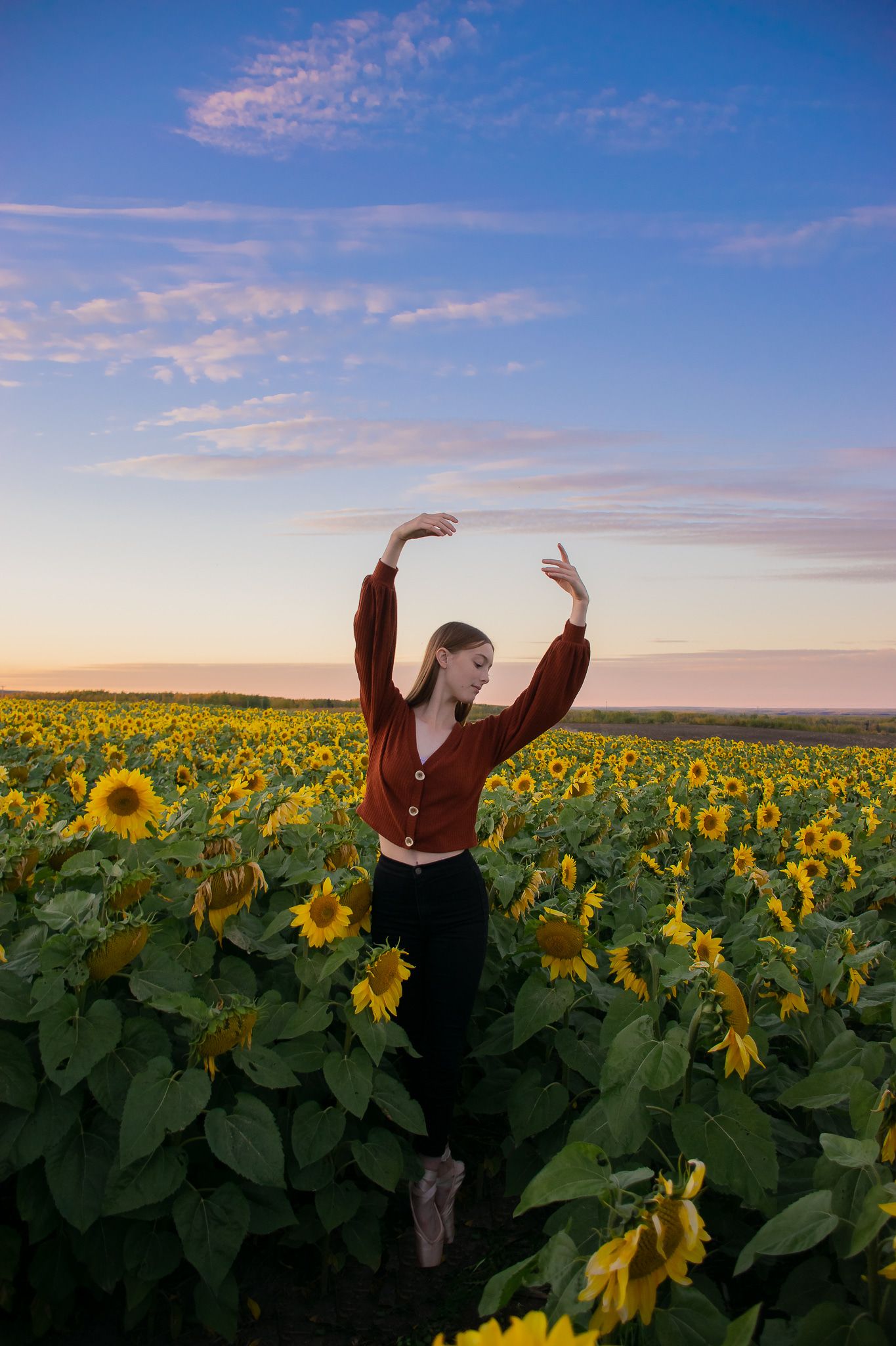 Silhouette of a person with raised arms dancing in a sunflower field at sunset.