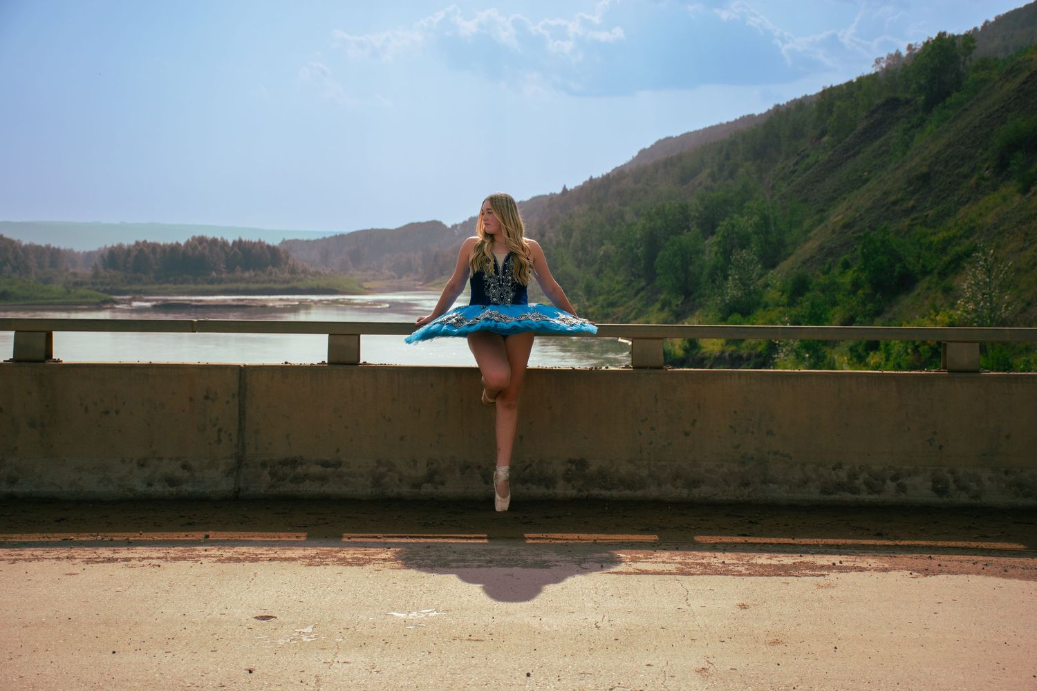Person in blue sits on concrete wall overlooking mountainous landscape.