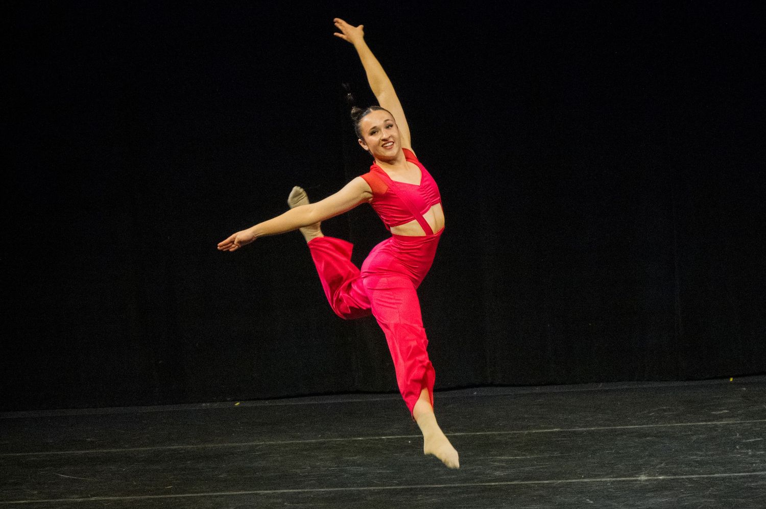 A ballet dancer in a flowing red dress performs a dramatic leap sequence across a dark stage.