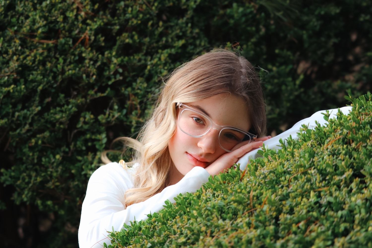 senior girl photoshoot, head resting on green bush
